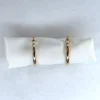 Gold hoop earrings depicted on a white cloth wrap with a speckled white background