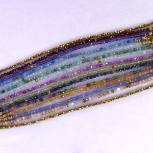 Various gold colored gemstone bracelets aligned horizontally on a speckled white background