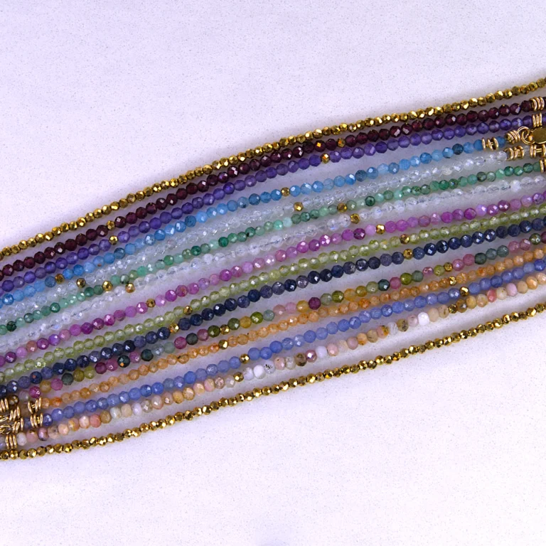 Various gold colored gemstone bracelets aligned horizontally on a speckled white background