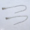 A set of sterling silver threader earrings with a sterling silver authentic charm on spotted white marble background