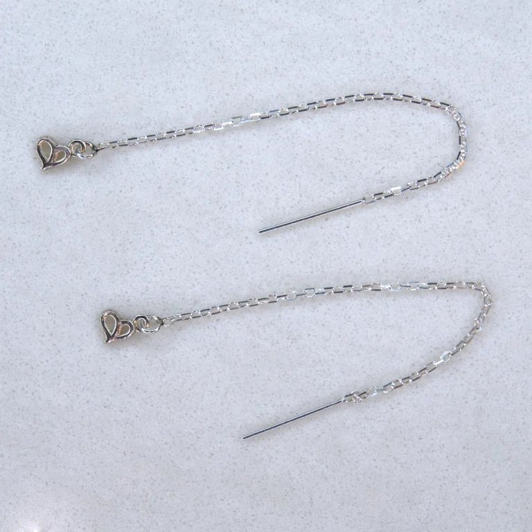 A set of sterling silver threader earrings with a sterling silver authentic charm on spotted white marble background