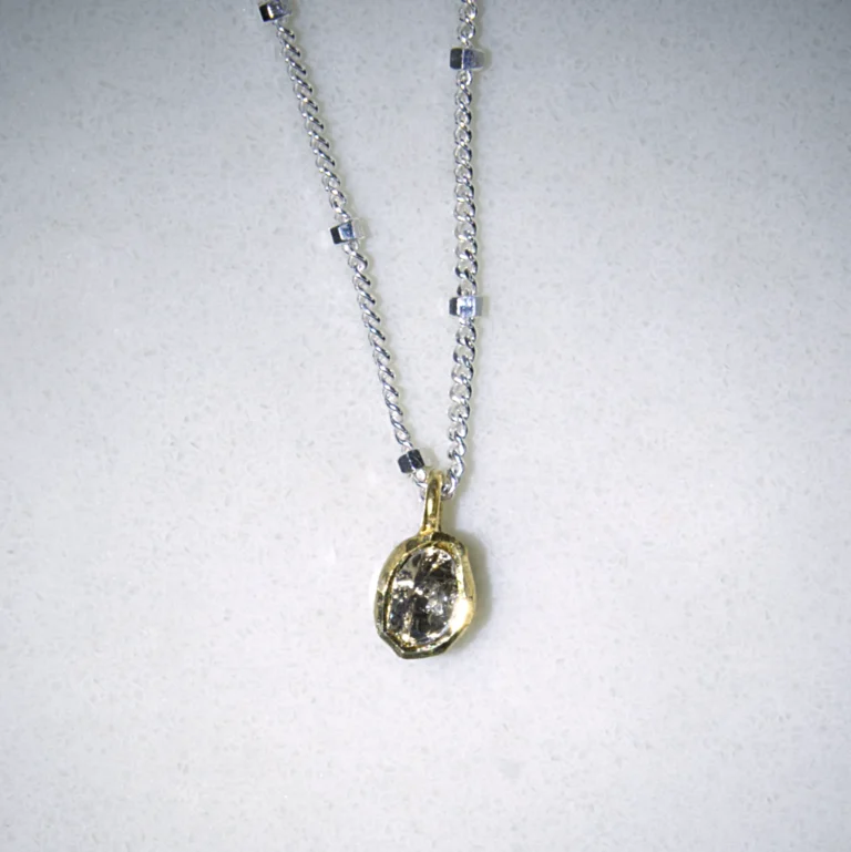 close up view sterling silver hope necklace with a gold vermeil polki diamond pendant on a white speckled background