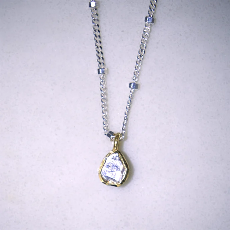 close up view sterling silver hope necklace with a gold vermeil polki diamond pendant on a white speckled background